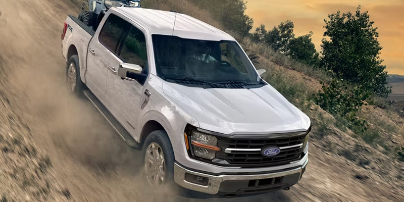 A white Ford pickup truck driving off-road through dusty terrain