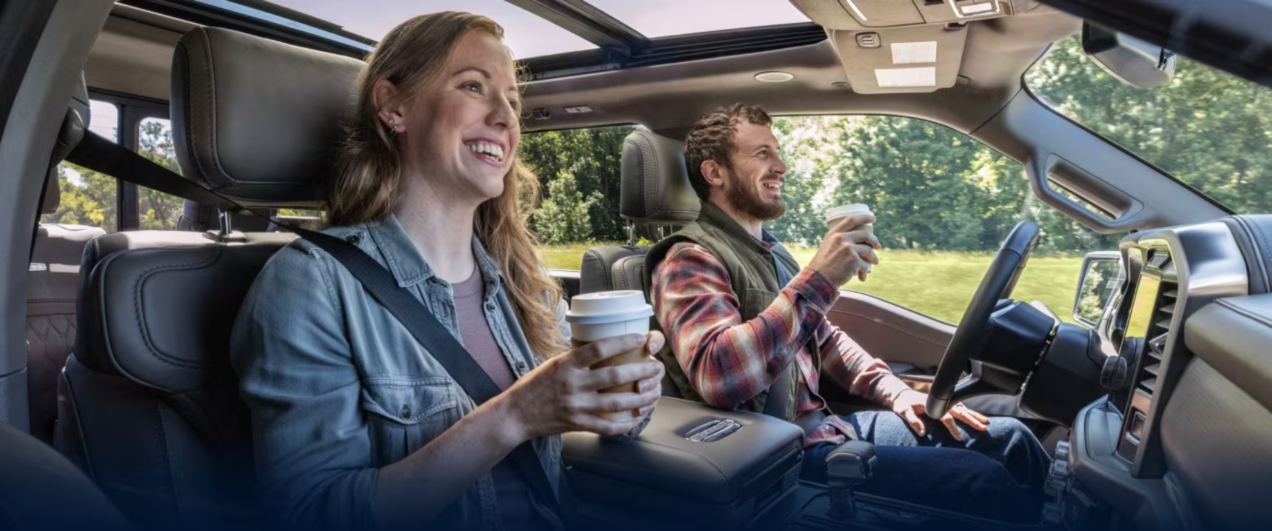 A man and woman smiling and holding coffee cups in a car