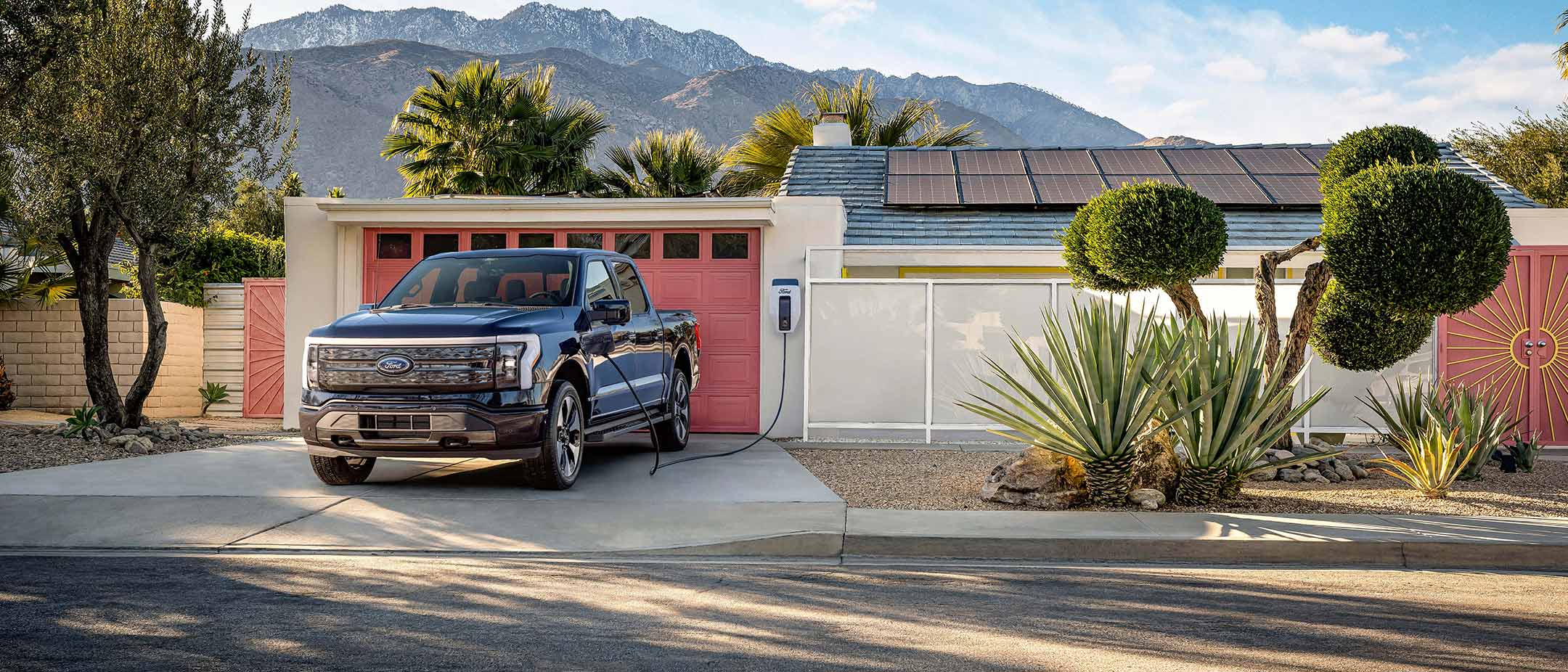 A Ford F-150 Lightning electric truck charging in front of a house with solar panels on the roof